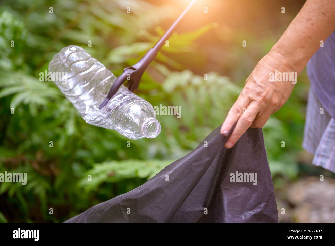 Primo piano della mano e del grabber che raccolgono i rifiuti di bottiglie di plastica in un sacchetto. Problemi ecologici e ambientali. Recycli Foto Stock