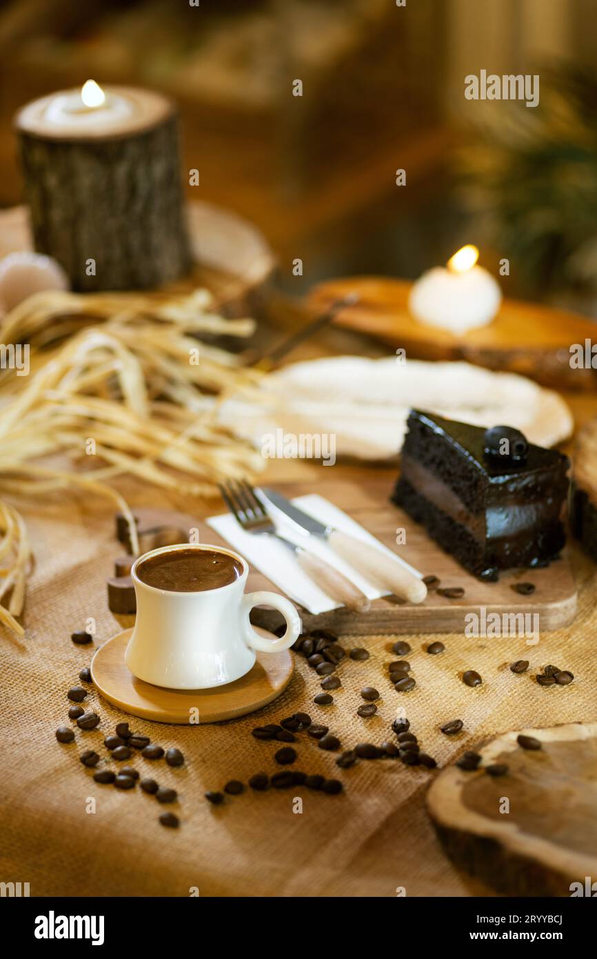 Una tazza di caffè turco è al centro del palcoscenico, completata da una fetta di torta al cioccolato, chicchi di caffè e illuminazione ambientale. Foto Stock