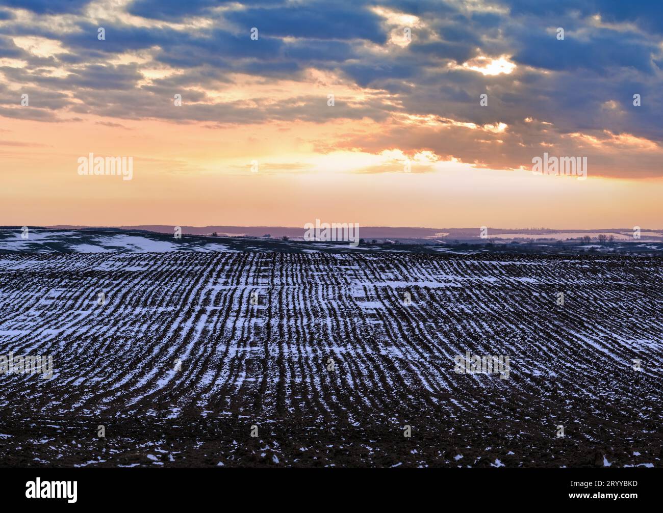 Terra nera, terra arabile coperta dall'ultima neve, primavera primaverile. Calmo tramonto serale nella campagna Ucraina, regione di Lviv Foto Stock