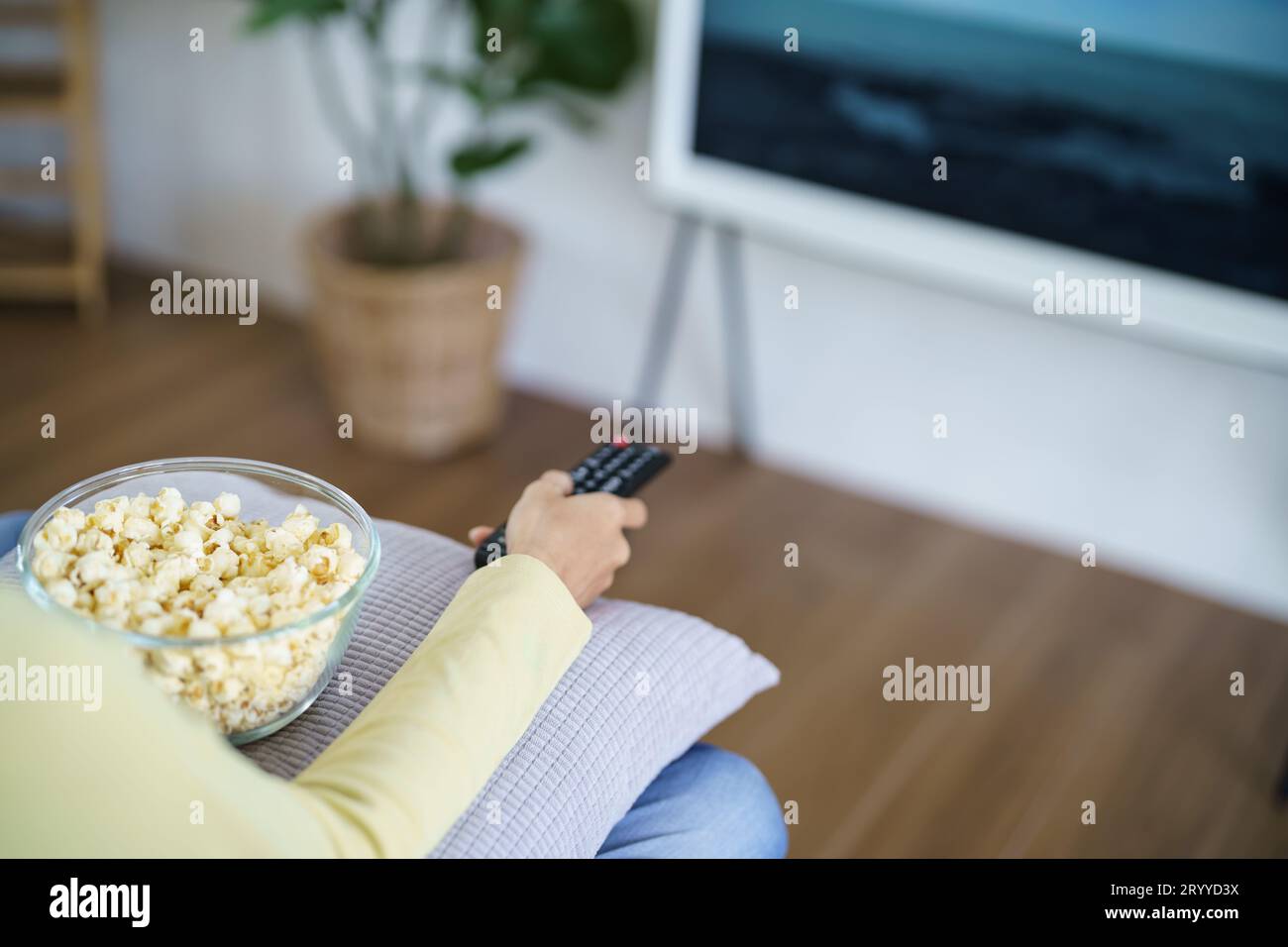 Donna asiatica che guarda la Smart TV e utilizza il telecomando tenendo il telecomando audio della televisione a casa con il telecomando Foto Stock