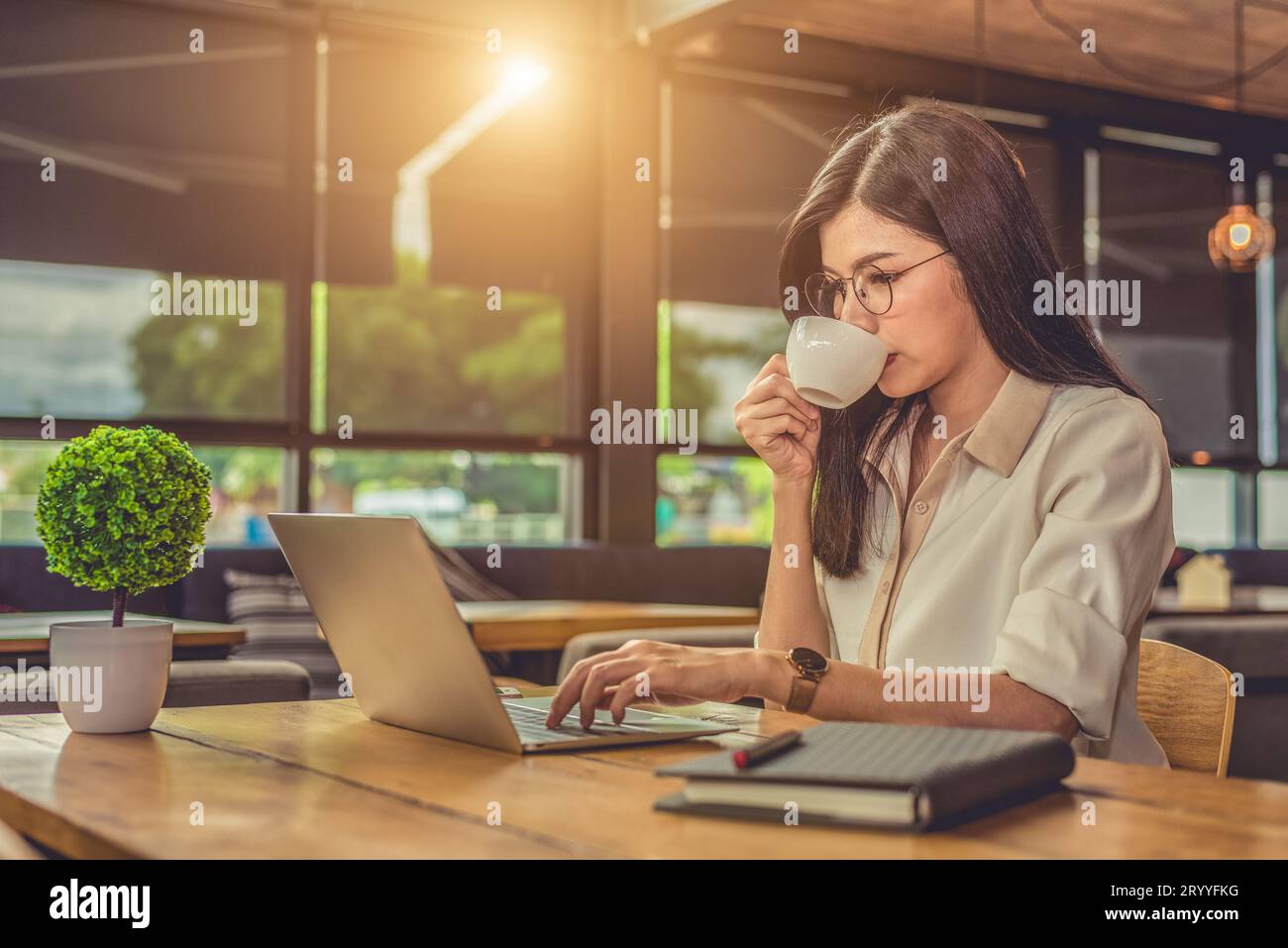 Lavoratrice asiatica che usa il computer portatile e beve caffè in caffetteria. Concetto di persone e stili di vita. Tecnologia e tema aziendale. Libero Foto Stock