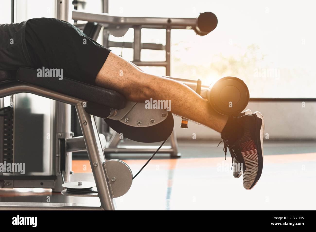 Primo piano dell'uomo sportivo che si allunga e solleva il peso con due gambe quando si guarda verso il basso per lo stretching muscolare nella palestra fitness del condominio Foto Stock