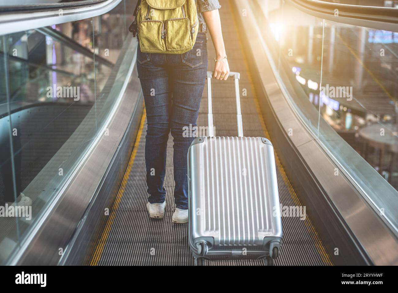 Vista posteriore della bella donna che viaggia e tiene la valigia sulla scala mobile in aeroporto. Concetto di persone e stili di vita. Viaggiare in giro per t Foto Stock