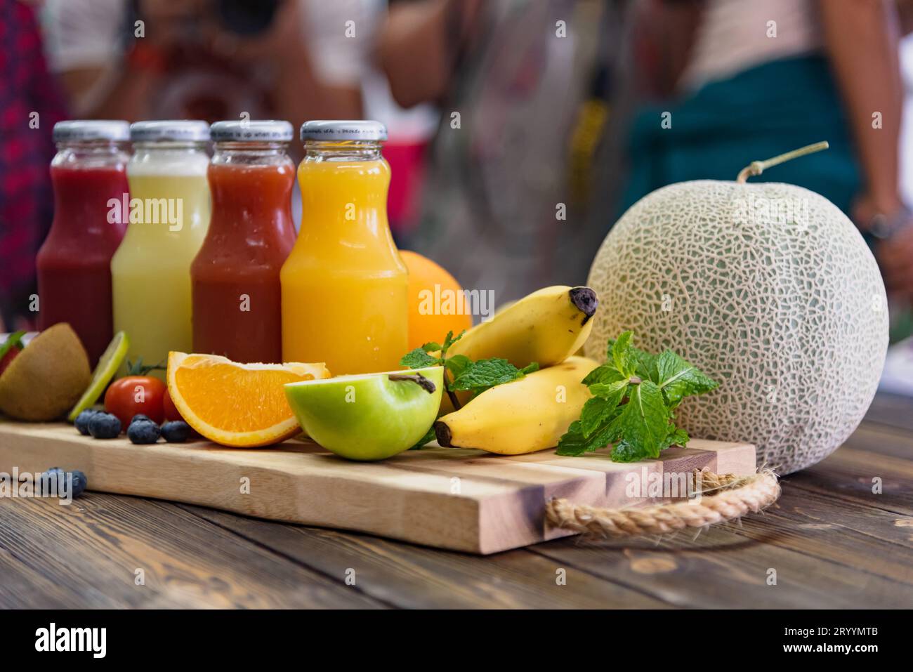 Frutta fresca e bottiglia di succo sul tavolo. Concetto di cibo e bevande. Cibo sano e vitamine c tema. Affollate le persone in background Foto Stock