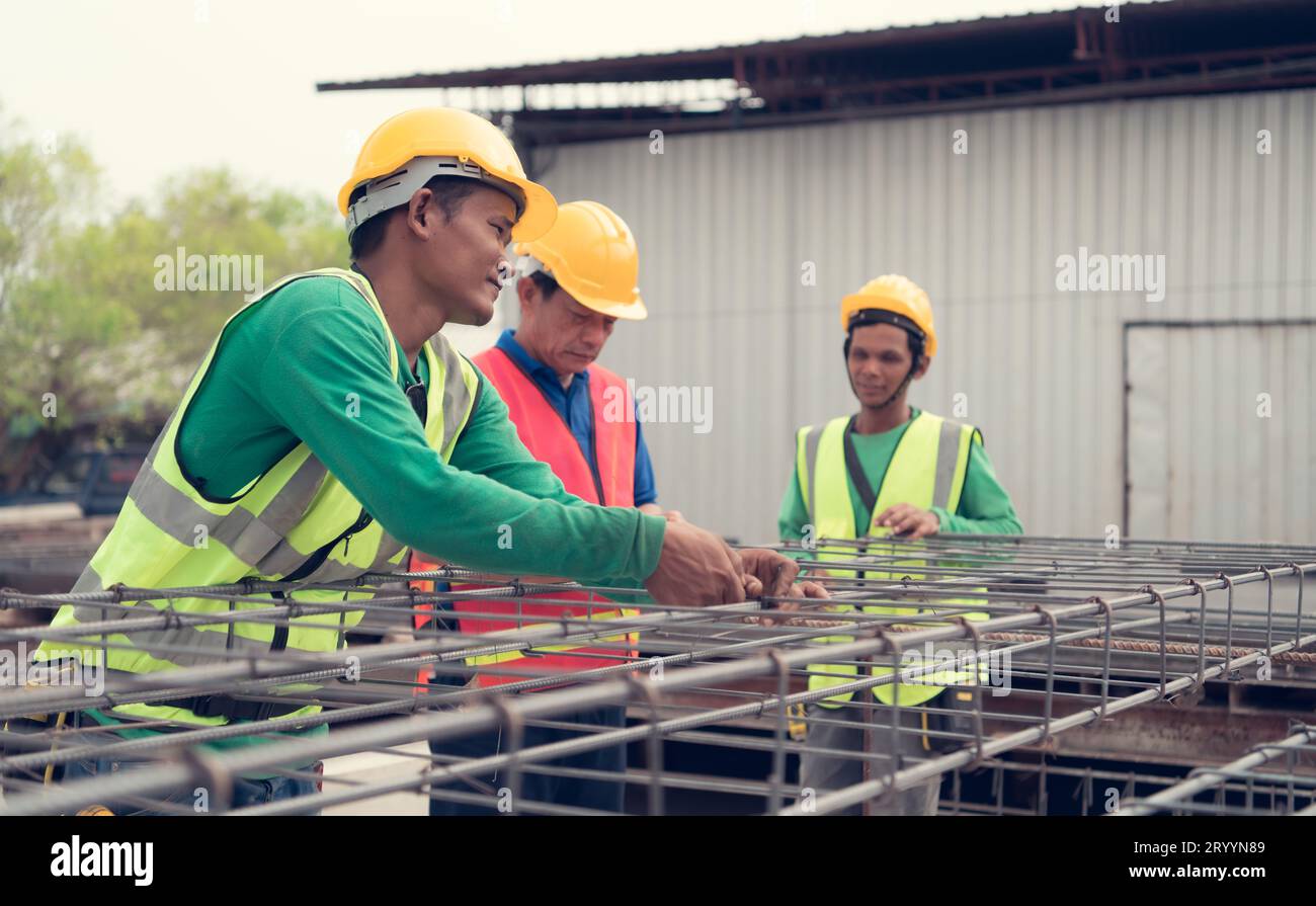 L'operaio edile sta legando saldamente l'acciaio strutturale c'è un supervisore che consiglia e supervisiona il lavoro da vicino. Foto Stock