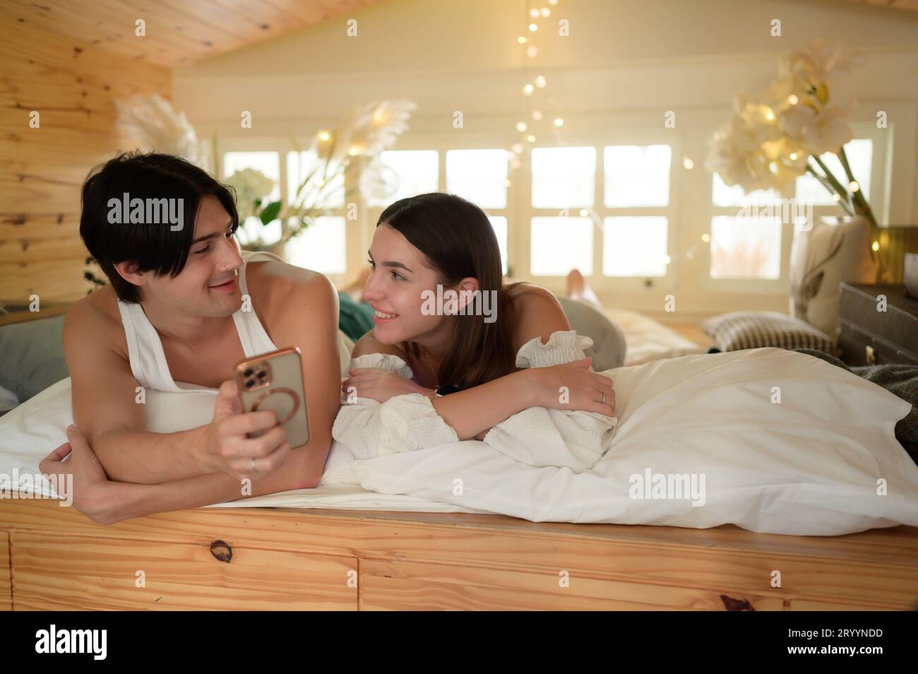Giovane coppia in soffitta la mattina, salutare gli amici online utilizzando lo smartphone. Foto Stock