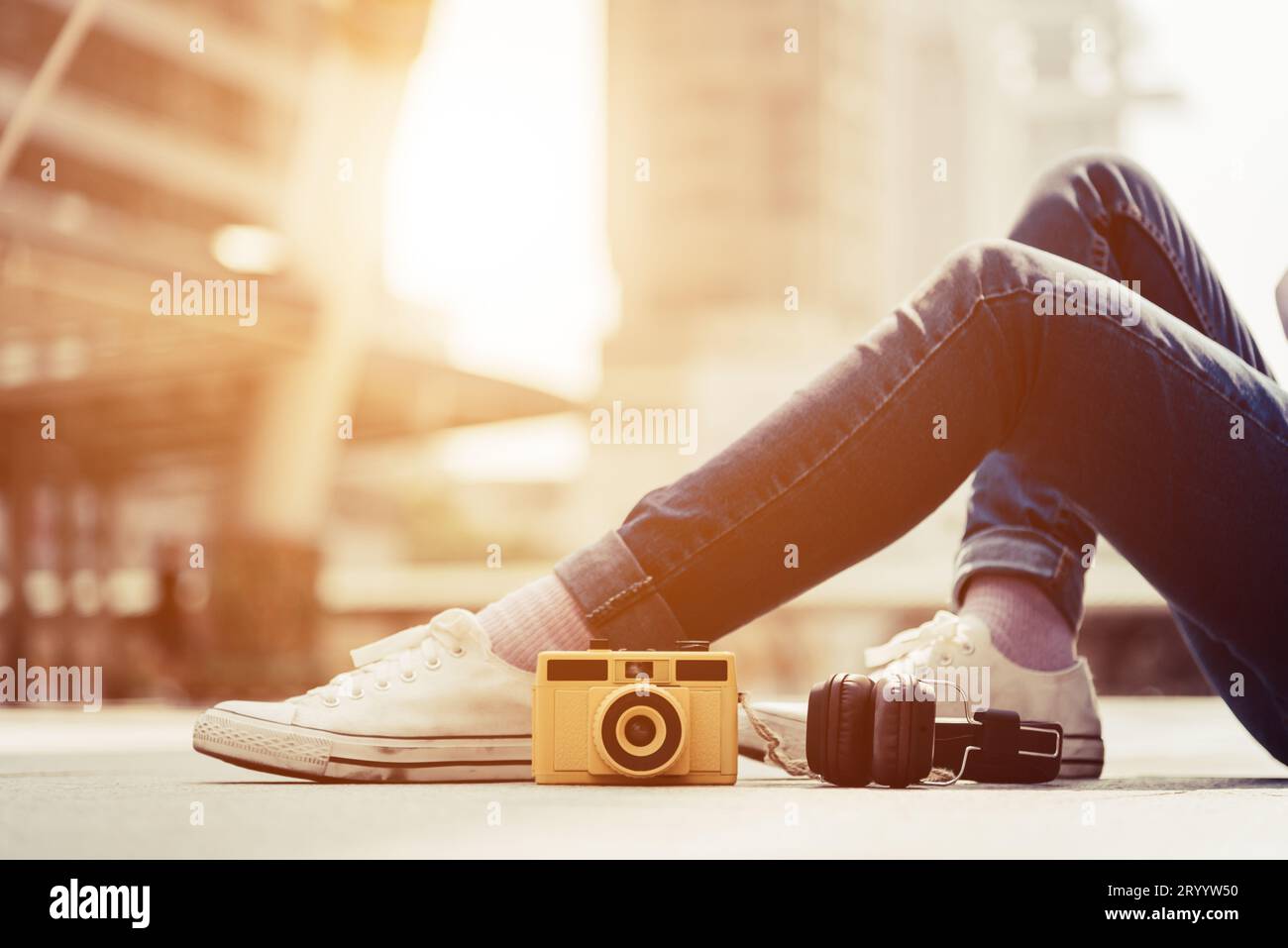 Le gambe delle donne indossano jeans e riposano e si rilassano nel centro della città. Fotocamera vintage e cuffie stereo elementi moda e modalità Foto Stock