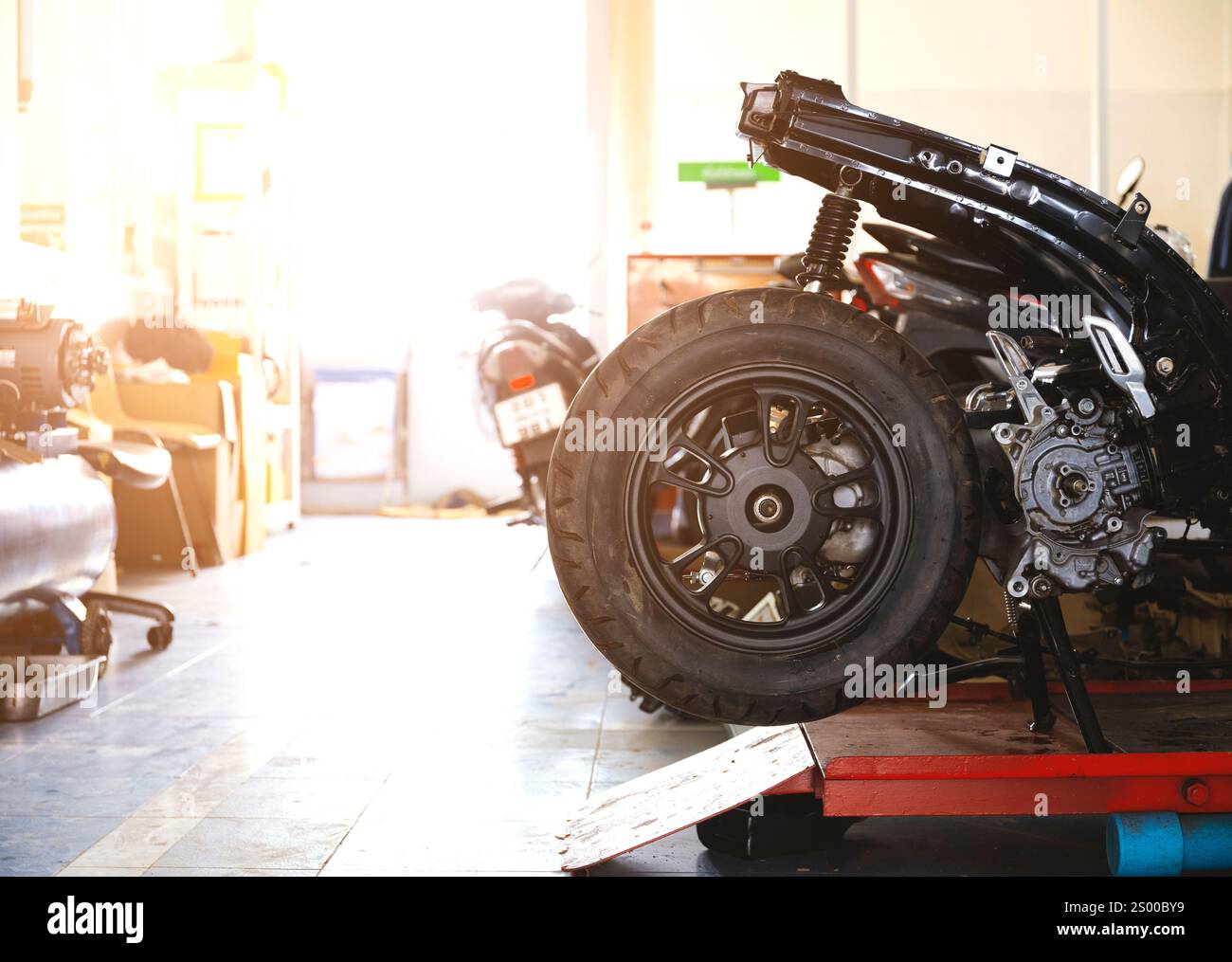 foto dettagliata di una ruota di una motocicletta su un ascensore rosso all'interno di un'officina, circondata da attrezzi e attrezzature sullo sfondo. Foto Stock