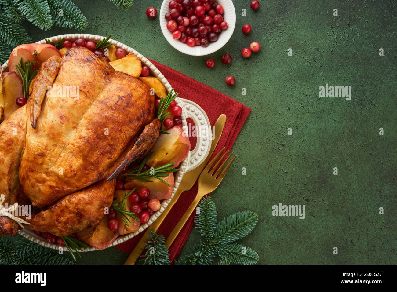 Pollo arrosto natalizio con mele, patate, mirtilli rossi, salsa ed erbe su un piatto grande su sfondo di marmo verde. Piatto natalizio di pollame per famiglie. Foto Stock