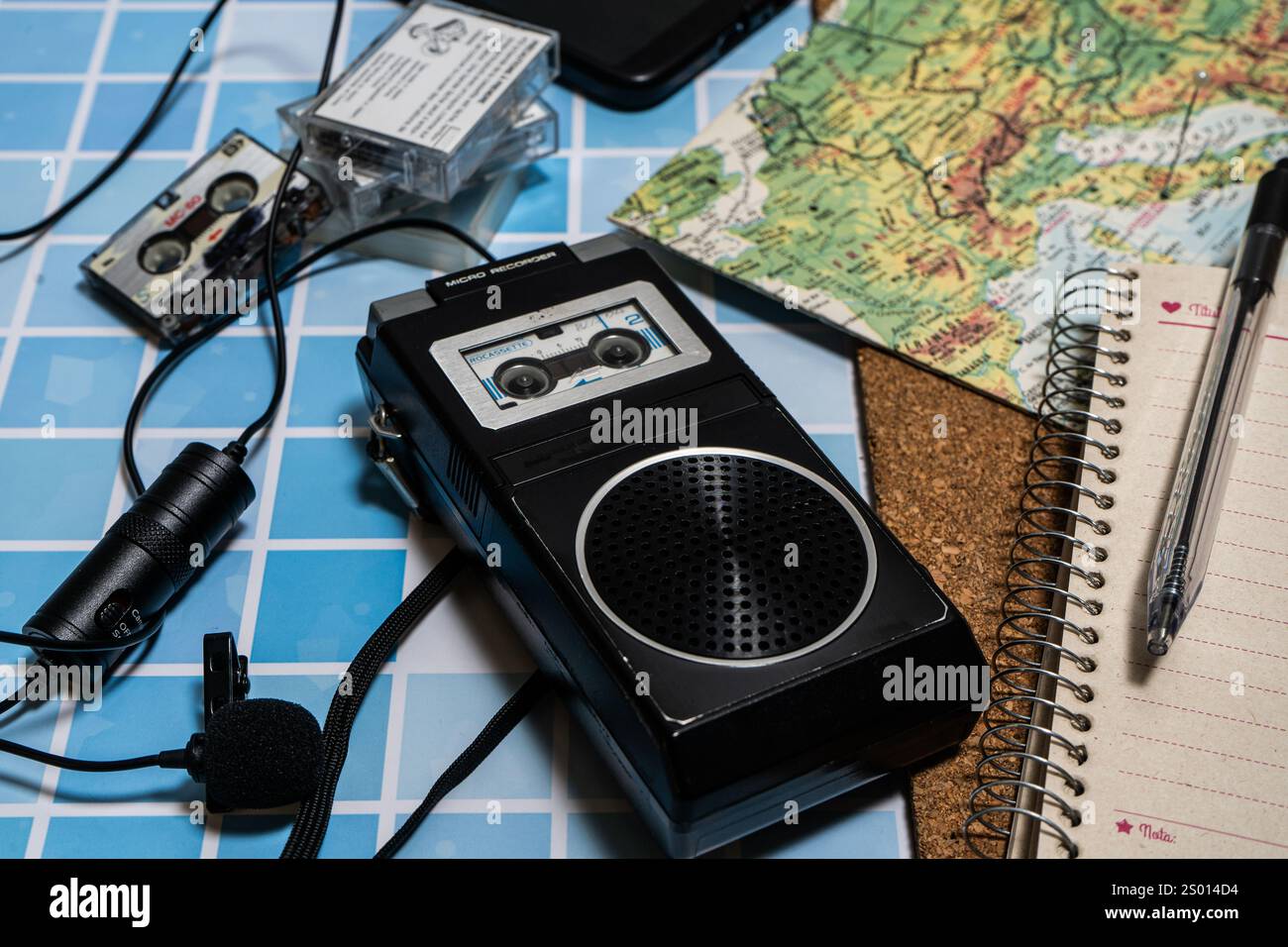 Vecchio registratore microcassette con microfono e diverse cassette accanto a una mappa. Attrezzatura da giornalista d'epoca. Foto Stock