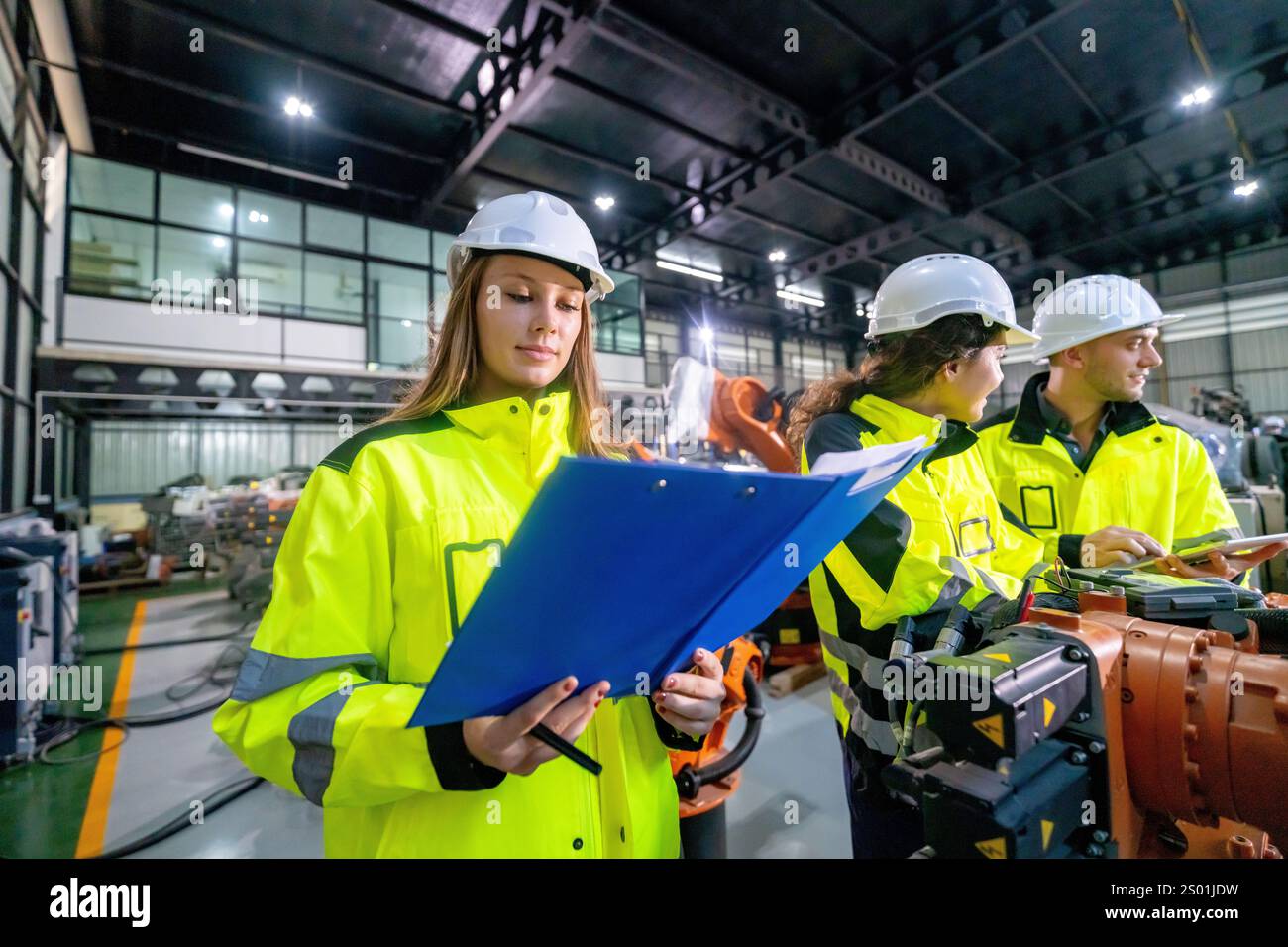 Il team di ingegneri che si occupano di dispositivi di sicurezza analizza i documenti in un moderno stabilimento di produzione pieno di attrezzature e macchinari mentre discute delle pubbliche relazioni in corso Foto Stock