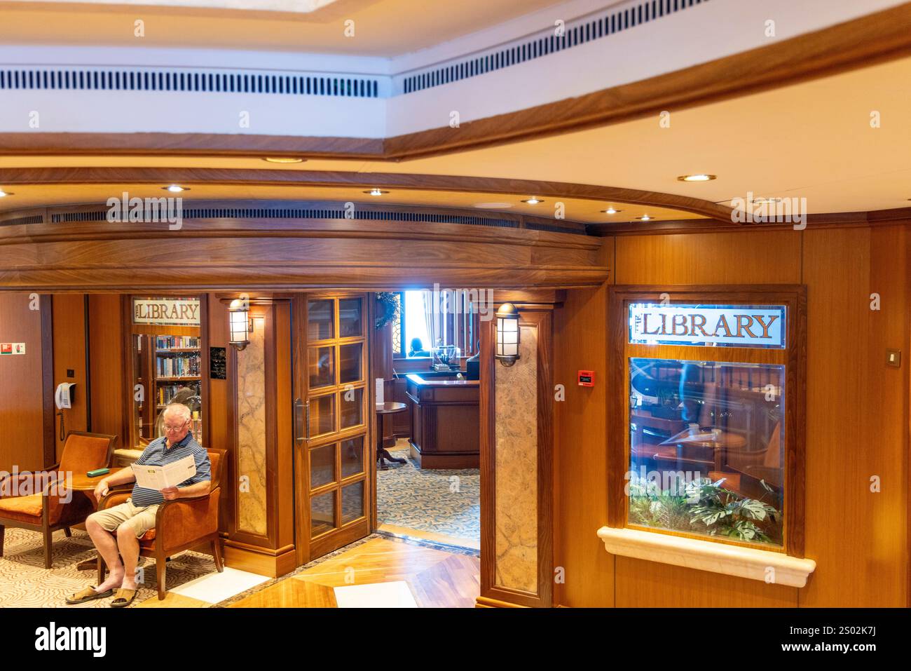 Nave da crociera Cunard Queen Elizabeth con la biblioteca delle navi sui ponti 2 e 3 con uomo seduto all'esterno, mentre la nave naviga nelle acque australiane Foto Stock