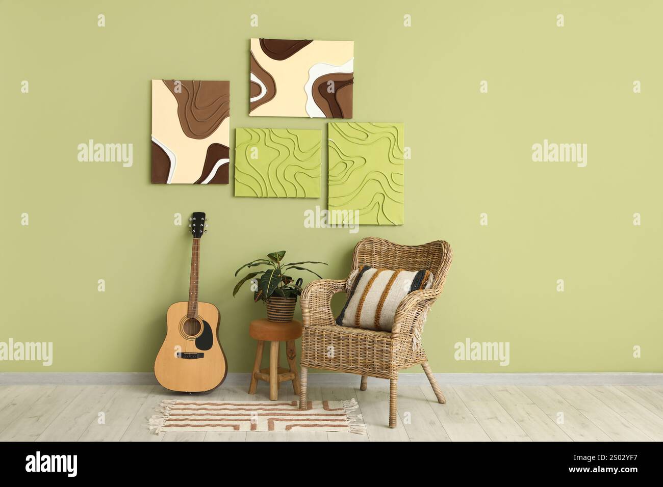 Poltrona Wicker, chitarra, piante d'casa e dipinti su parete verde in camera Foto Stock