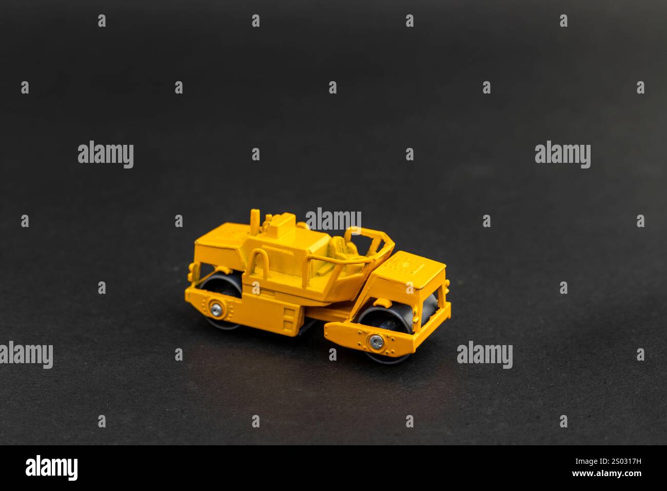 Modello giocattolo con rullo per asfalto giallo su sfondo nero Foto Stock