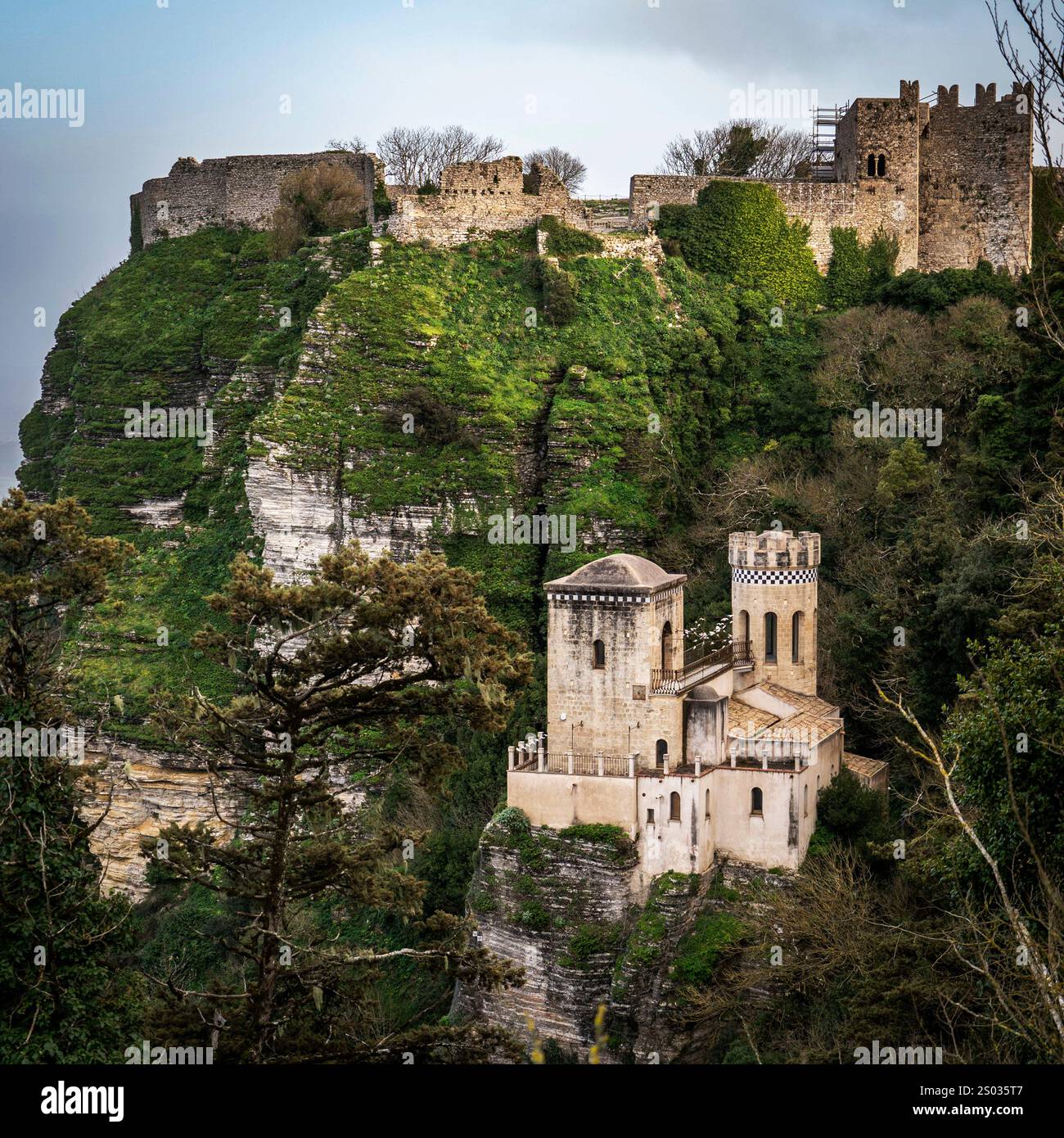 Una vista panoramica di un castello medievale arroccato su una scogliera, circondato da vegetazione lussureggiante. Il castello presenta un mix di strutture in pietra, con un prominente To Foto Stock