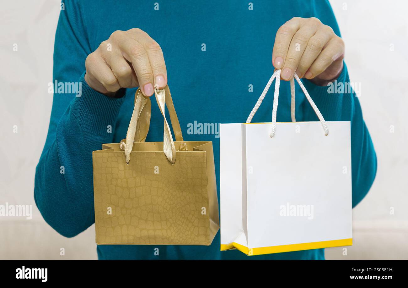 La persona tiene in mano due borse della spesa, una piccola in oro e una bianca più grande, indicando un recente viaggio di shopping all'interno. Foto Stock