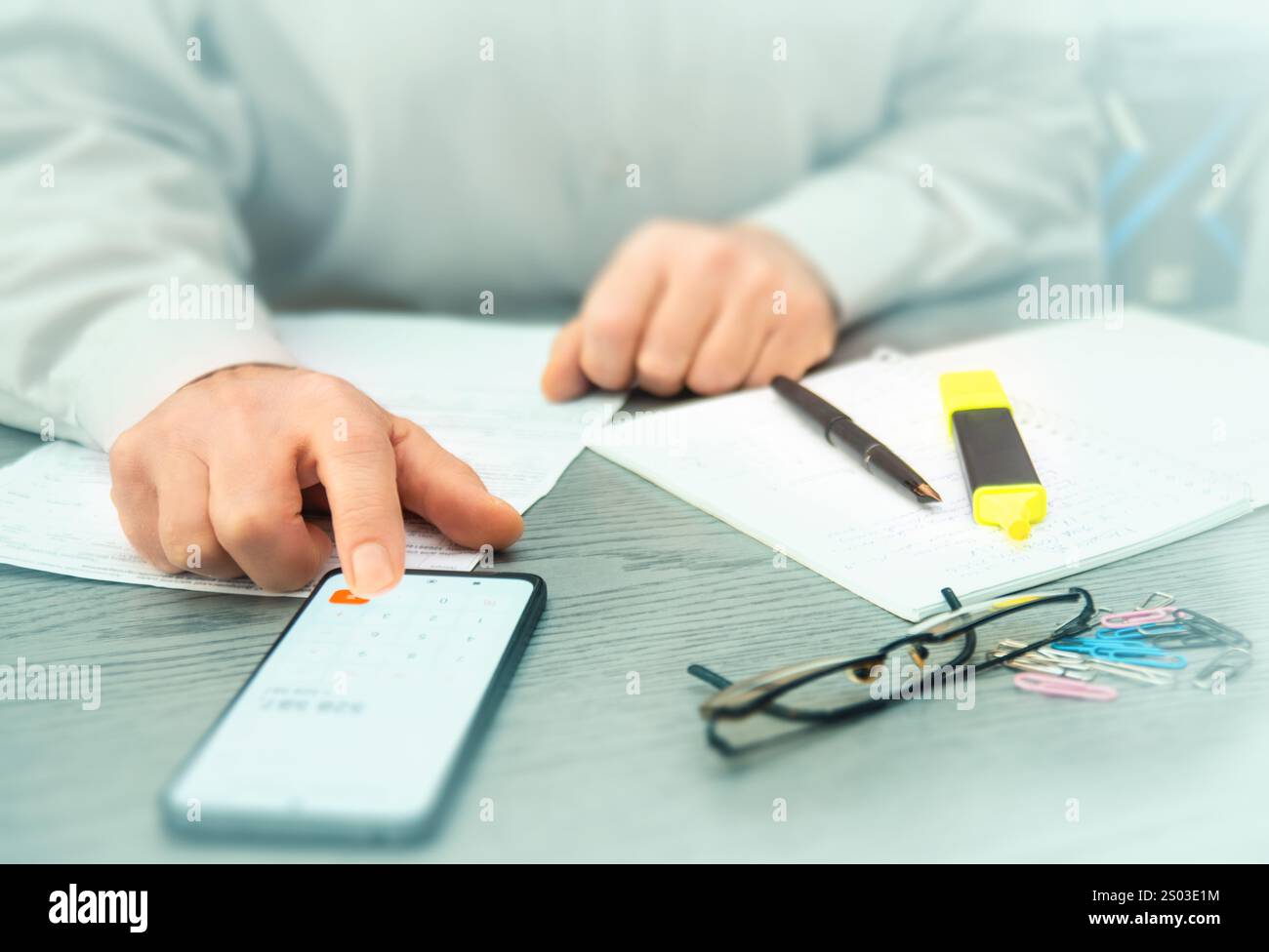 Una persona esamina i dati delle criptovalute su uno smartphone e prende appunti mentre analizza le tendenze di mercato in un ambiente d'ufficio contemporaneo. Foto Stock