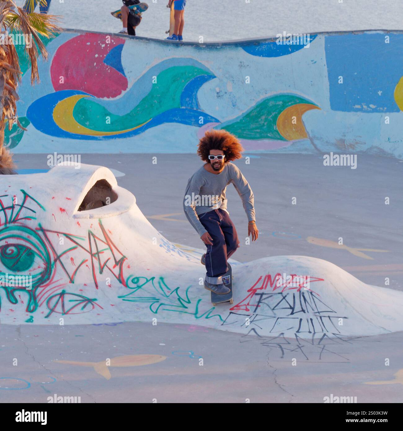 Un giovane uomo figo con capelli grandi e occhiali da sole su Skate Board presso uno Skate Park nel villaggio di Taghazout, Marocco. 23 dicembre 2024 Foto Stock