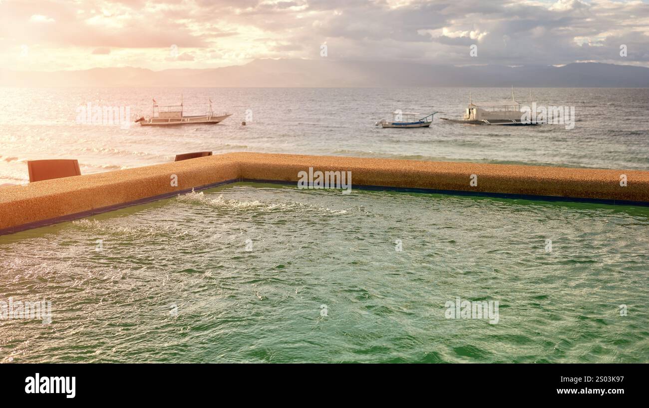 Piscina fronte spiaggia al tramonto, focalizzazione selettiva sull'acqua, Filippine. Foto Stock