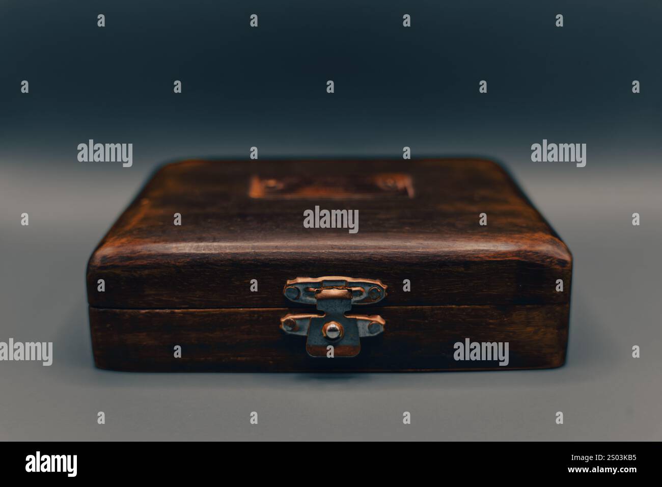 Primo piano di un'antica scatola di legno con chiusura in metallo e texture rustica, catturata su uno sfondo a gradiente neutro. Foto Stock