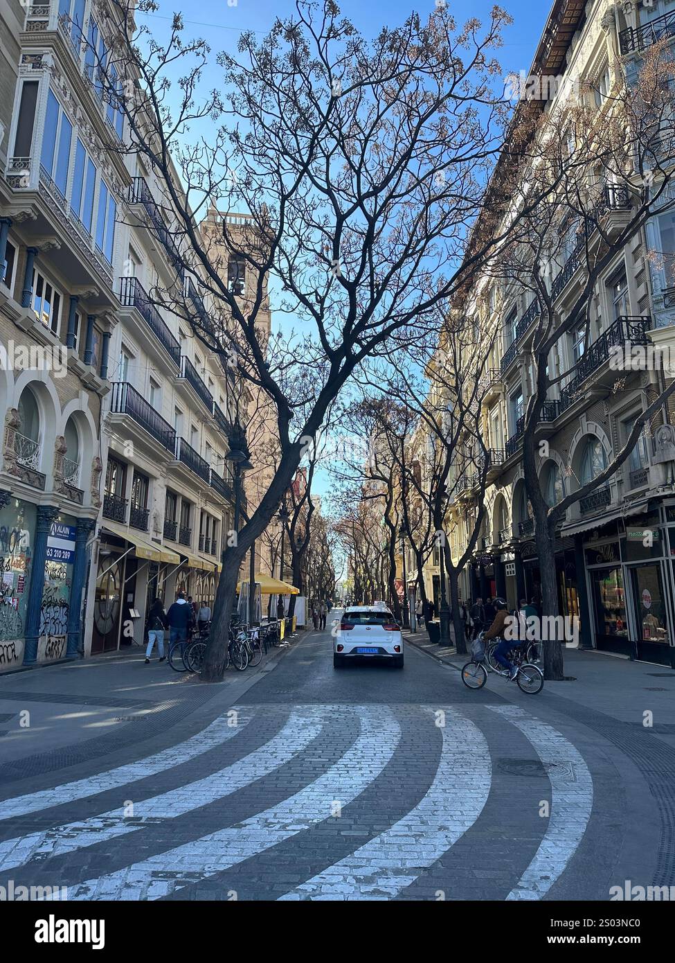 Rue pittoresque à Valence, Espagne, bordée d’arbres et d’immeubles historiques avec balcons en fer forgé. Scène typique d’une ville européenne animée. Foto Stock