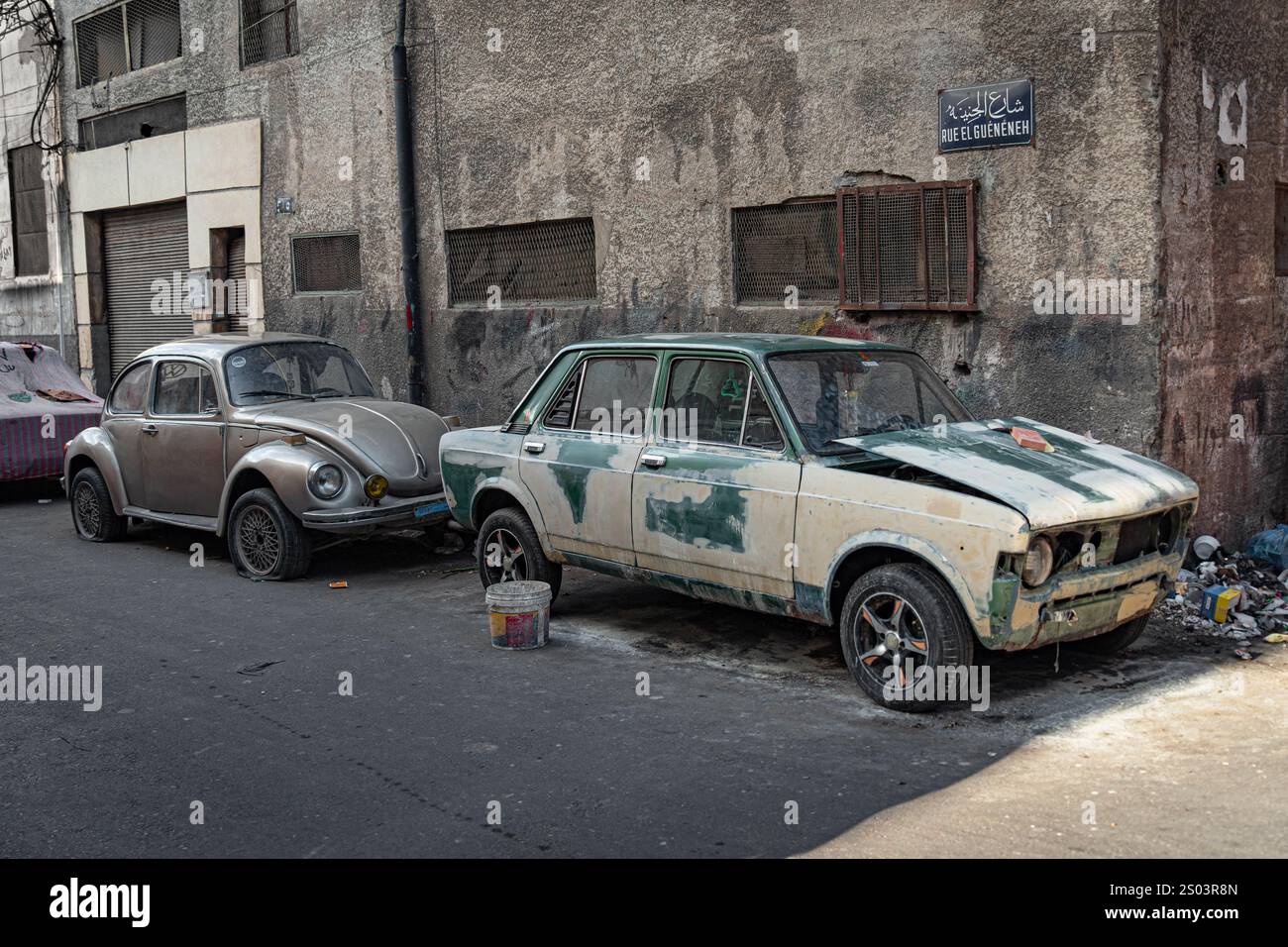 Una strada di Alexandria presenta una vecchia auto preparata per la pittura, accanto a un Maggiolino Volkswagen d'epoca. La scena mette in risalto la maestria urbana. Foto Stock