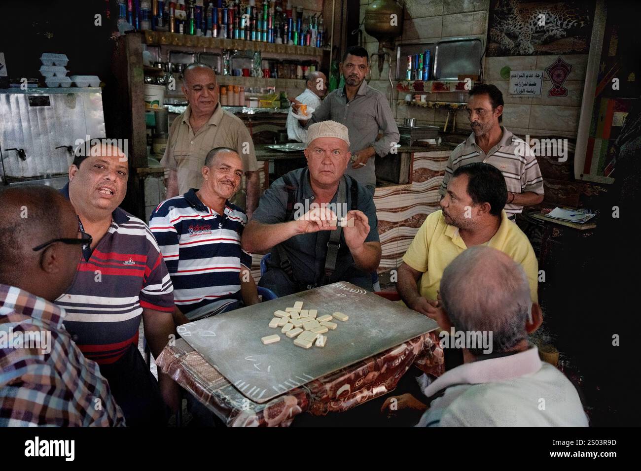 Un vivace raduno di uomini egiziani che giocano a domino e si godono il tè in una caffetteria tradizionale ad Alessandria, in Egitto. La scena riflette il cameratismo Foto Stock