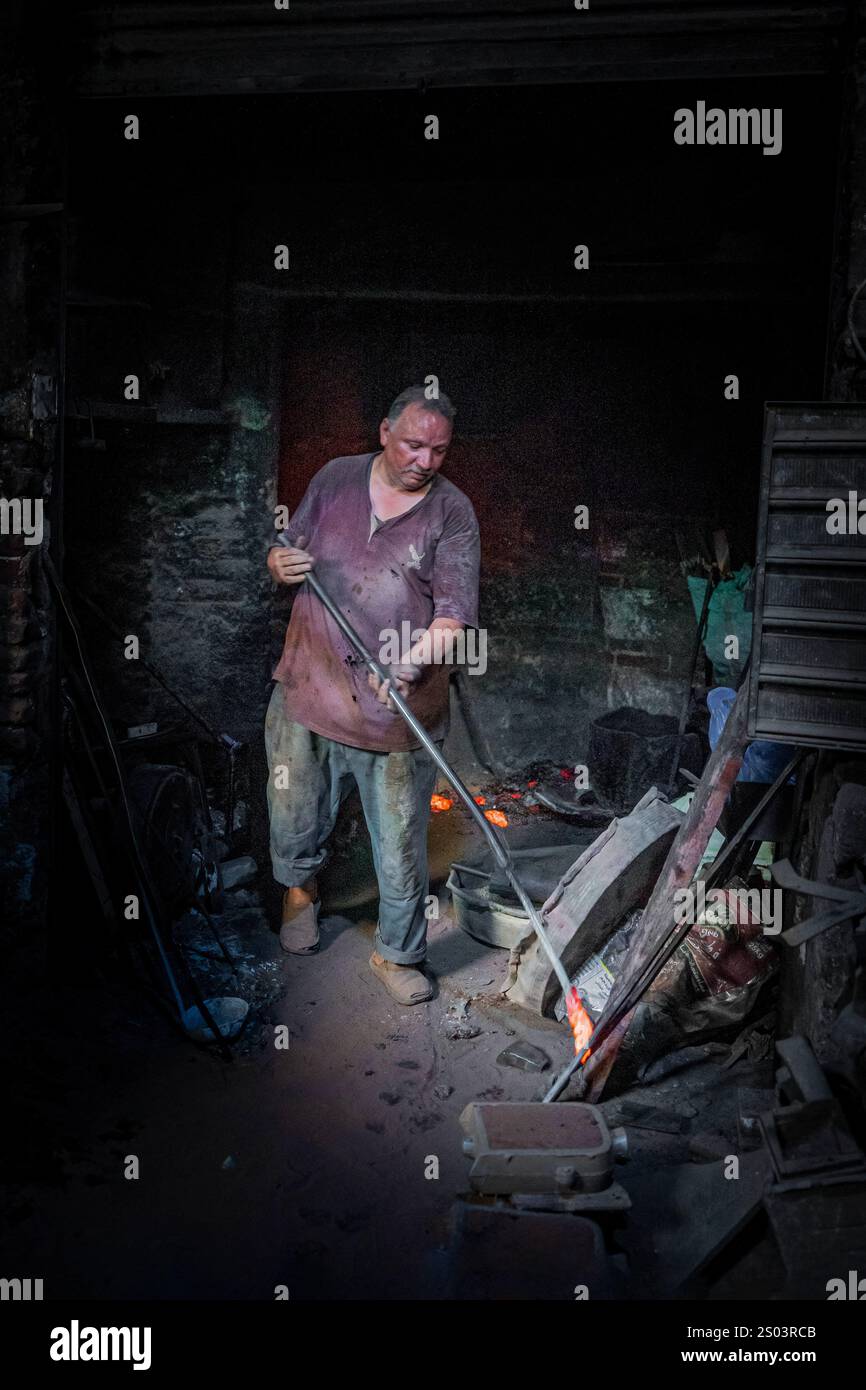 Un operaio di fonderia in un'officina ad Alessandria, Egitto, che fonde metallo fuso in un ambiente tradizionale. Un'immagine del fondatore dell'ottone riflette l'artigianato locale Foto Stock