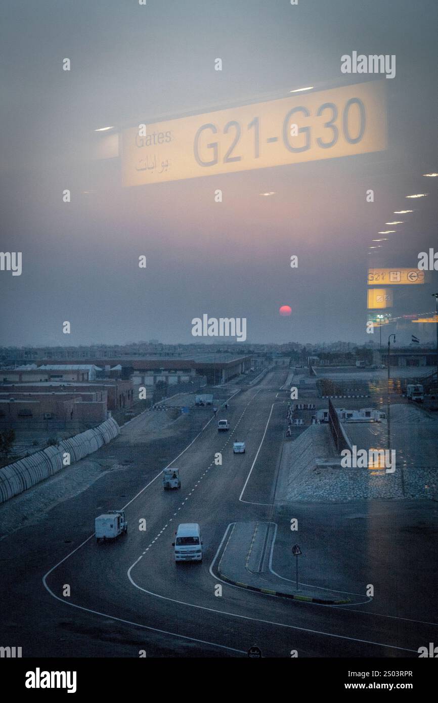 Aeroporto di Alessandria, Egitto, catturato al crepuscolo attraverso una finestra di vetro. La vista evidenzia una strada tranquilla con un cartello per le porte G21-G30 Foto Stock