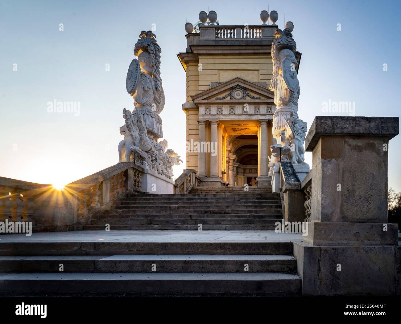Una grande scalinata che conduce ad un edificio ornato con sculture su entrambi i lati, illuminate dal caldo bagliore del sole che tramonta. Foto Stock