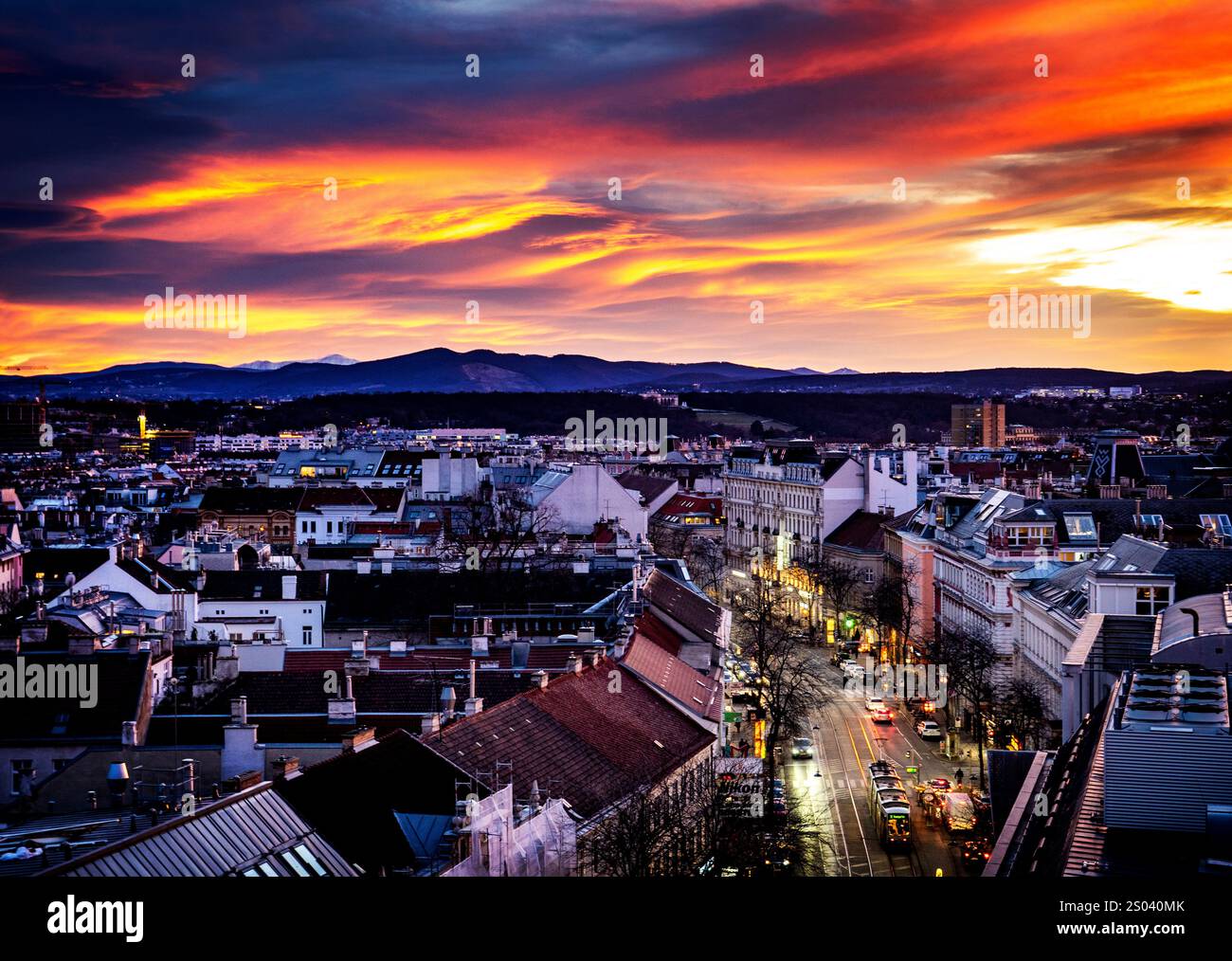 Uno splendido tramonto su un paesaggio urbano, con tetti e strade illuminate da una luce calda. Il cielo è pieno di arancione, rosa e viola vibranti Foto Stock
