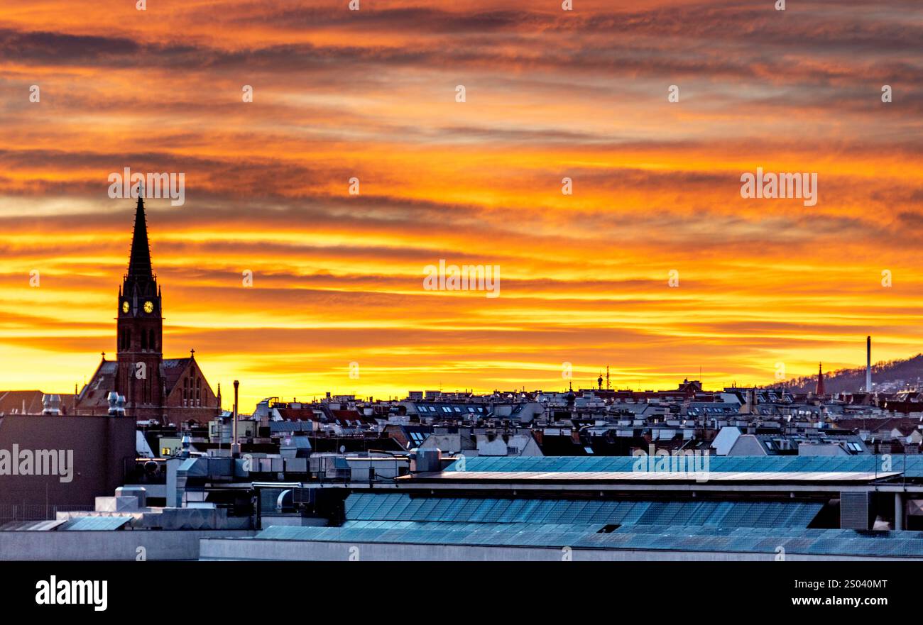 Uno splendido tramonto sullo skyline della città con tetti e un'importante torre della chiesa. Il cielo è pieno di vivaci tonalità arancio e giallo, creato Foto Stock