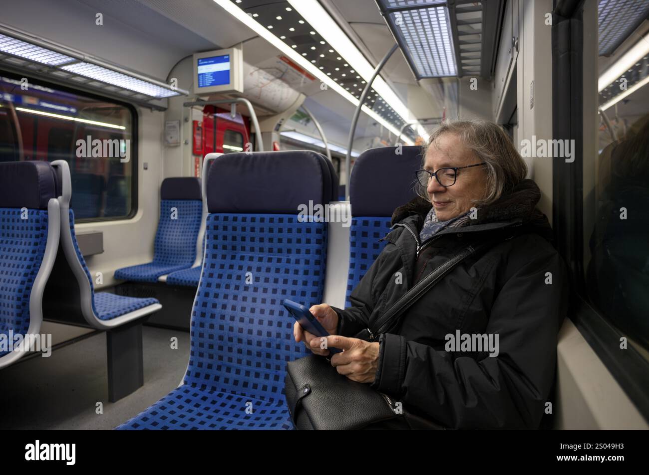 Donna anziana seduta in treno suburbano, treno, uso del telefono cellulare, smartphone, sorridente, Stoccarda, Baden-Wuerttemberg, Germania, Europa Foto Stock