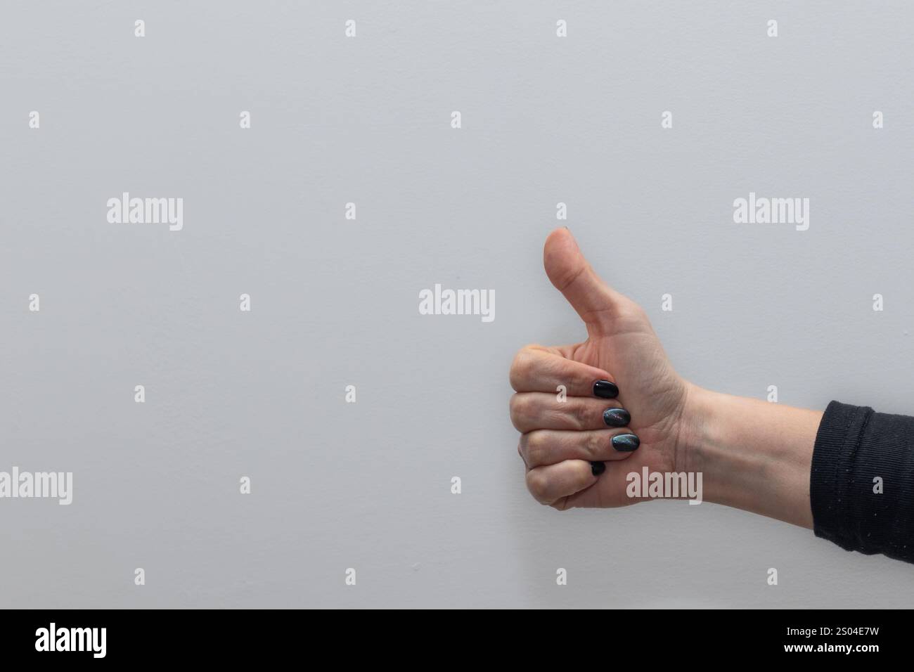 La mano di una donna con un dito sollevato, su un semplice sfondo grigio, segnalando il numero uno o la posizione del primo posto Foto Stock