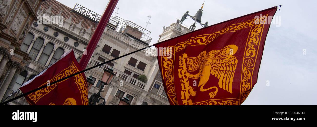 VENEZIA, ITALIA - 5 MAGGIO 2015: Panorama della Torre dell'Orologio in Piazza San Marco visto attraverso le bandiere del Leone alato Foto Stock