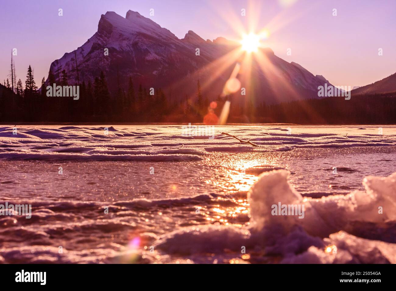 Un bellissimo tramonto su un lago con montagne sullo sfondo. Il sole splende brillantemente, creando un'atmosfera calda e tranquilla Foto Stock