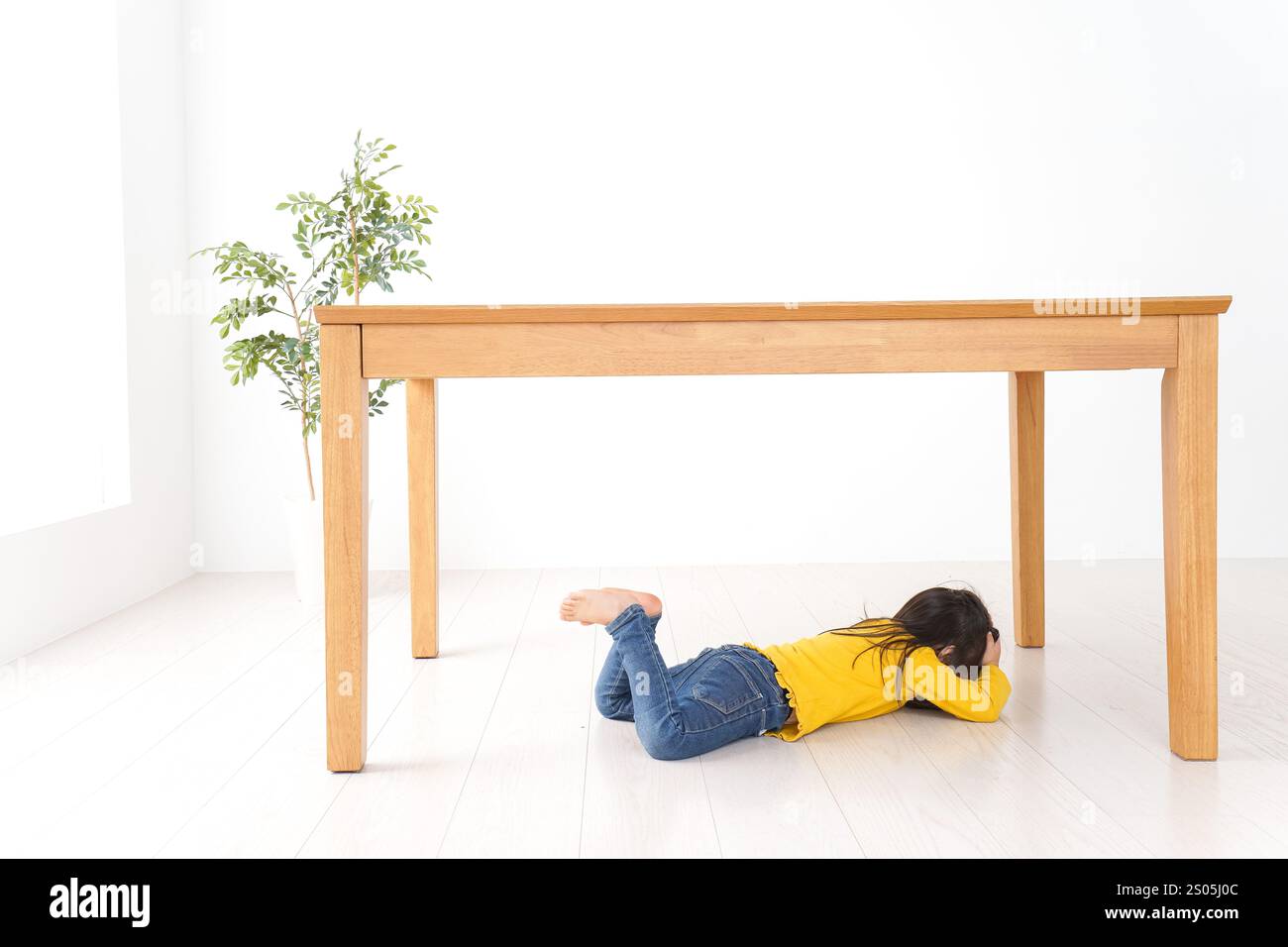 Bambino che si rifugia sotto una scrivania Foto Stock