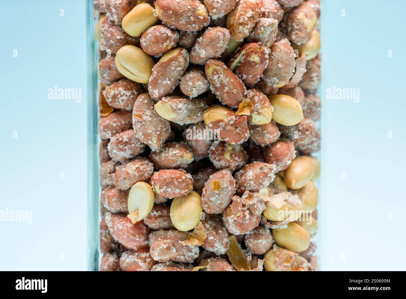 Arachidi salate riempite in vaso di vetro su sfondo blu Foto Stock