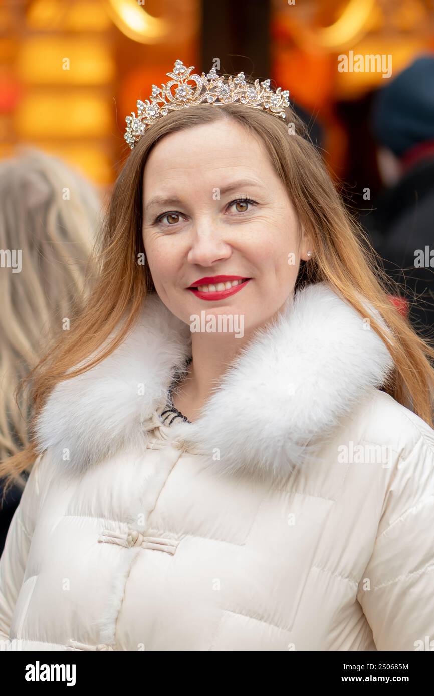 Una donna con i capelli lunghi e una tiara posa in una città vivace decorata con decorazioni e luci festose che creano un'atmosfera festosa. Foto Stock