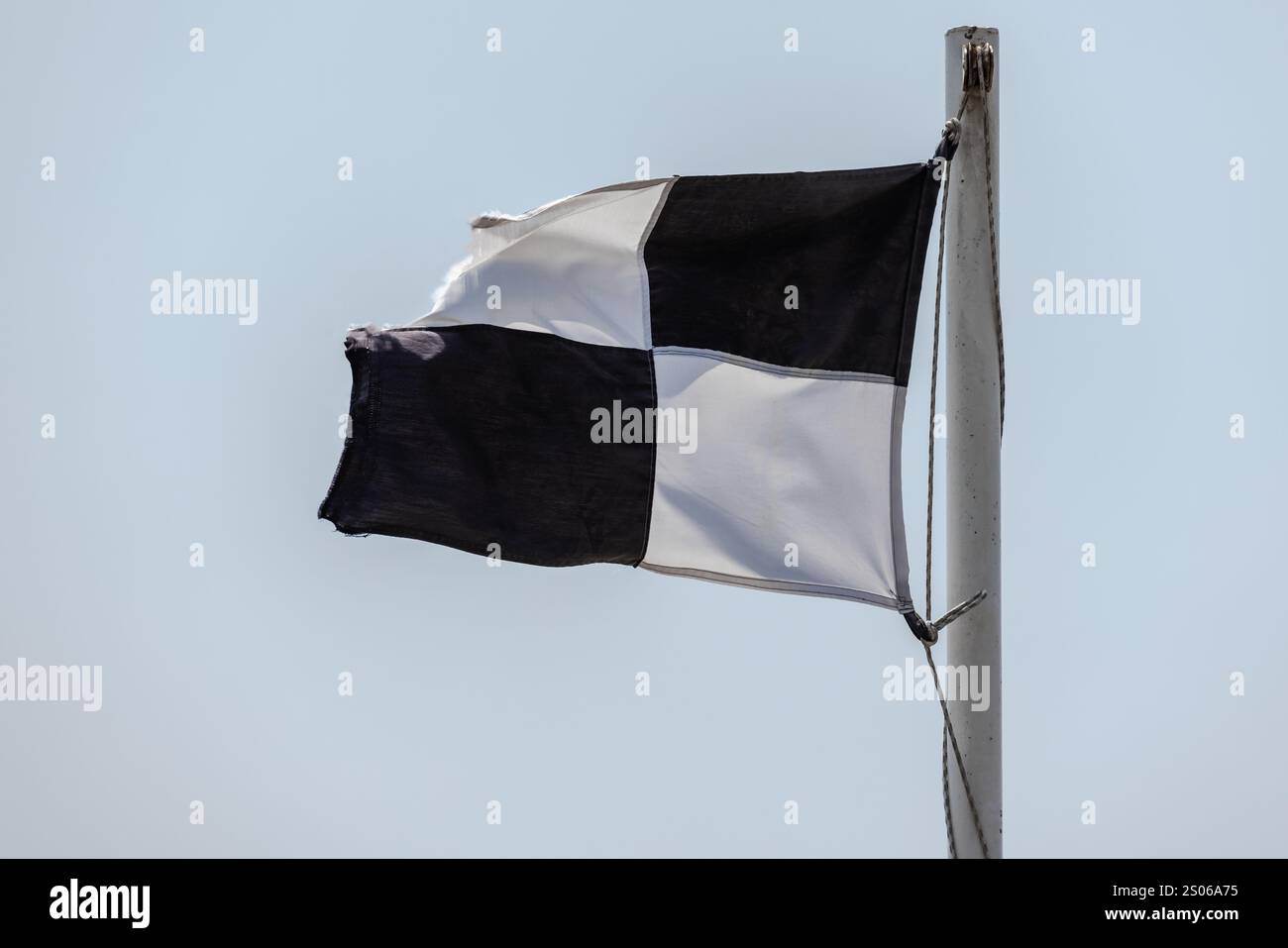 La bandiera della spiaggia, che avverte la dama bianca e nera, si trova sotto uno sfondo blu brillante Foto Stock