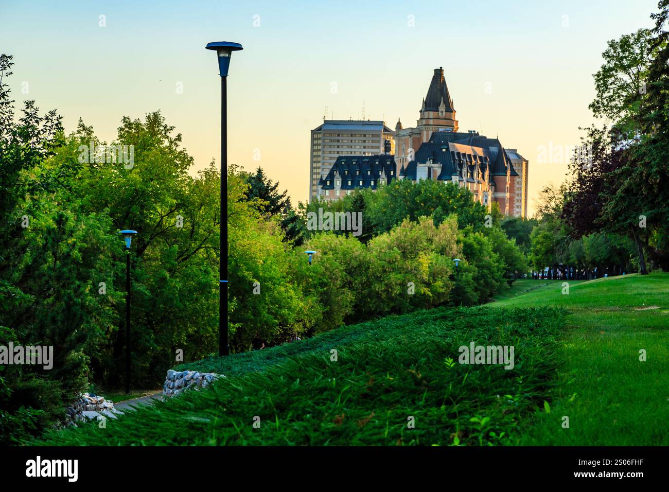 Un parco con un alto edificio sullo sfondo. Il cielo è blu e il sole sta tramontando Foto Stock