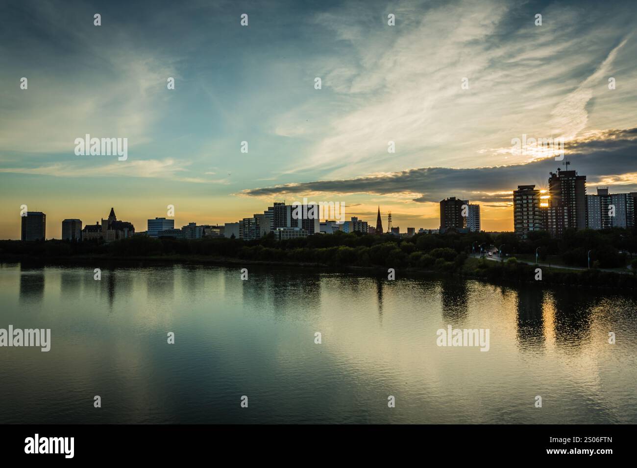 Lo skyline della città si riflette in un lago calmo al tramonto. Il cielo è pieno di nuvole, creando un'atmosfera serena e tranquilla Foto Stock