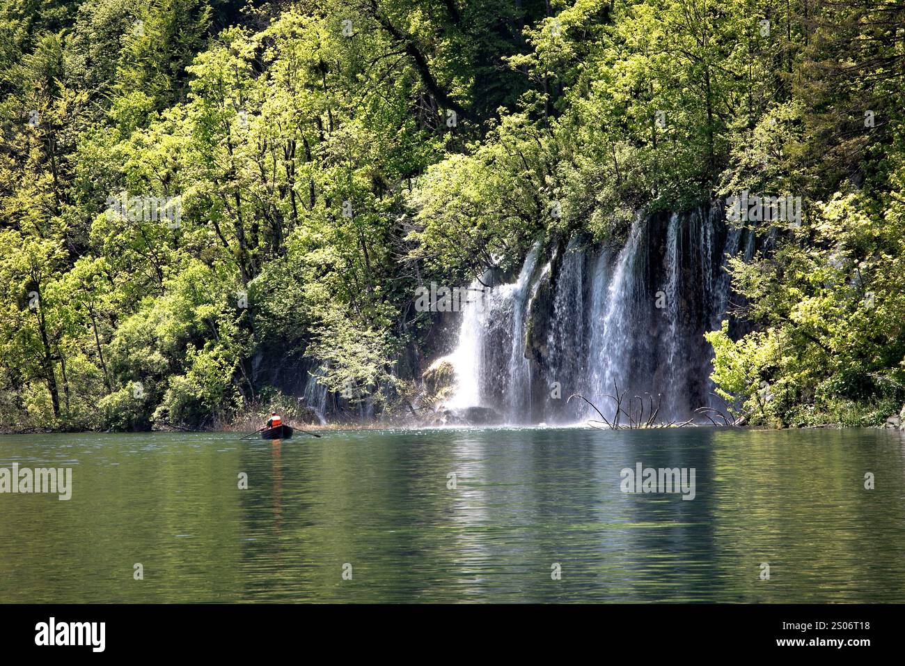 Un visitatore ammira la bellezza di una cascata incorniciata da una vegetazione lussureggiante nel Parco Nazionale dei Laghi di Plitvice, in Croazia, dove la tranquillità della natura e la tranquillità Foto Stock