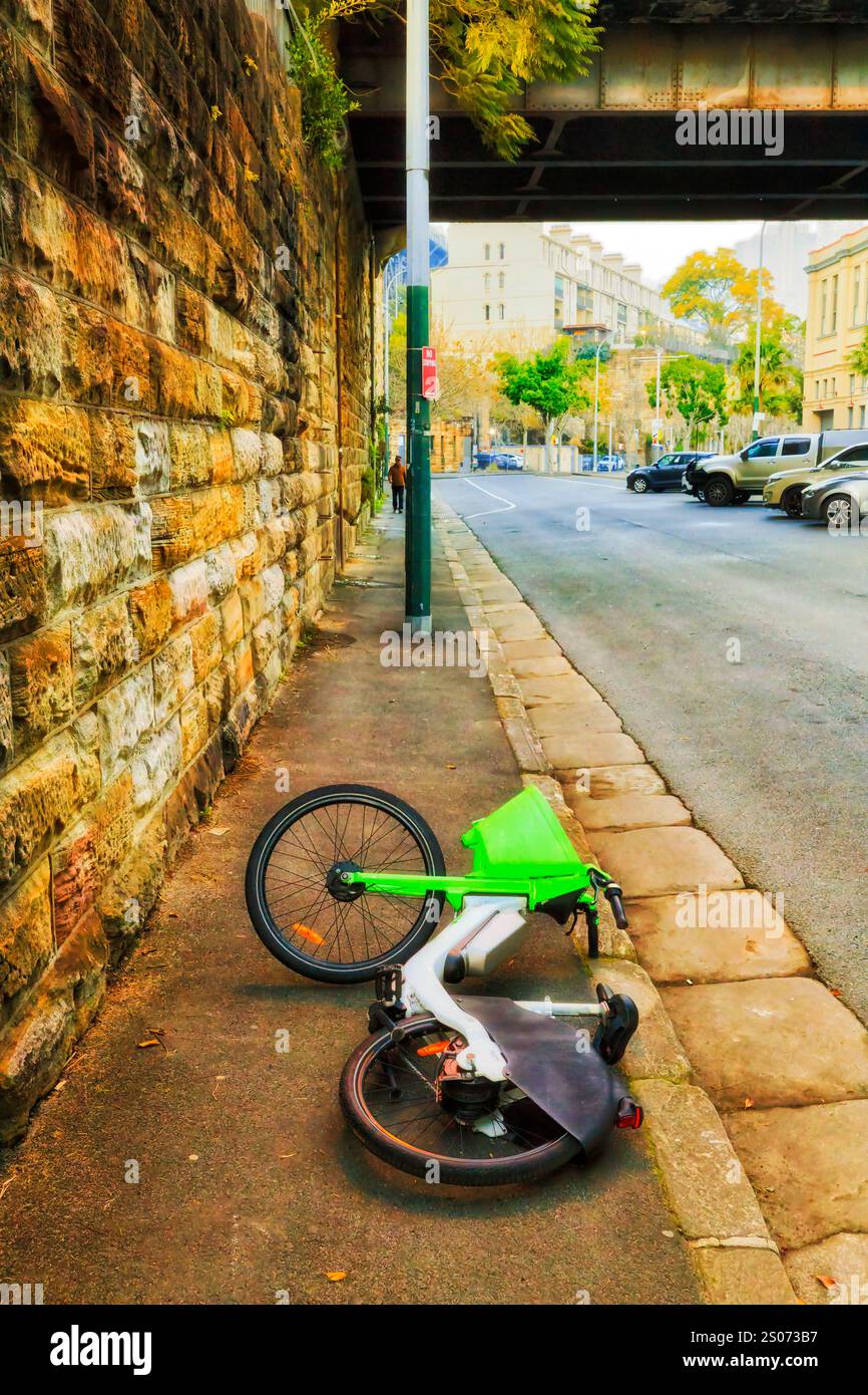 Bicicletta elettrica verde persa rotta adagiata sulla strada della città di Sydney, il quartiere Rocks in Australia - Gig Economy. Foto Stock