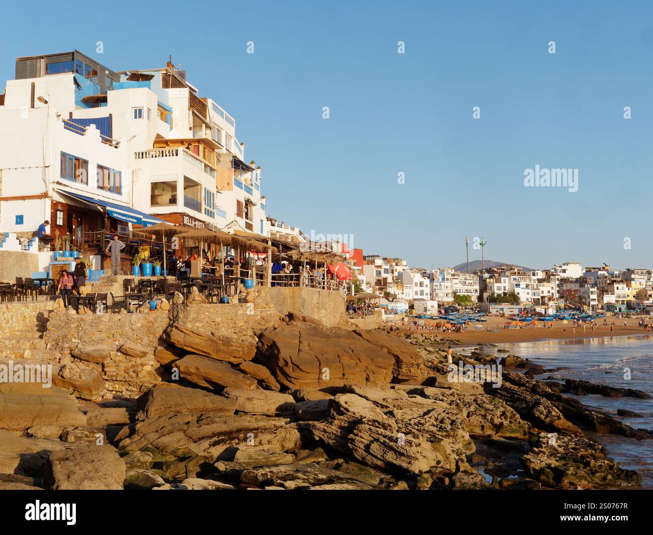 Spiaggia rocciosa e sabbiosa con ristoranti e barche da pesca blu nel villaggio di Taghazout, Marocco. 25 dicembre 2024. Foto Stock