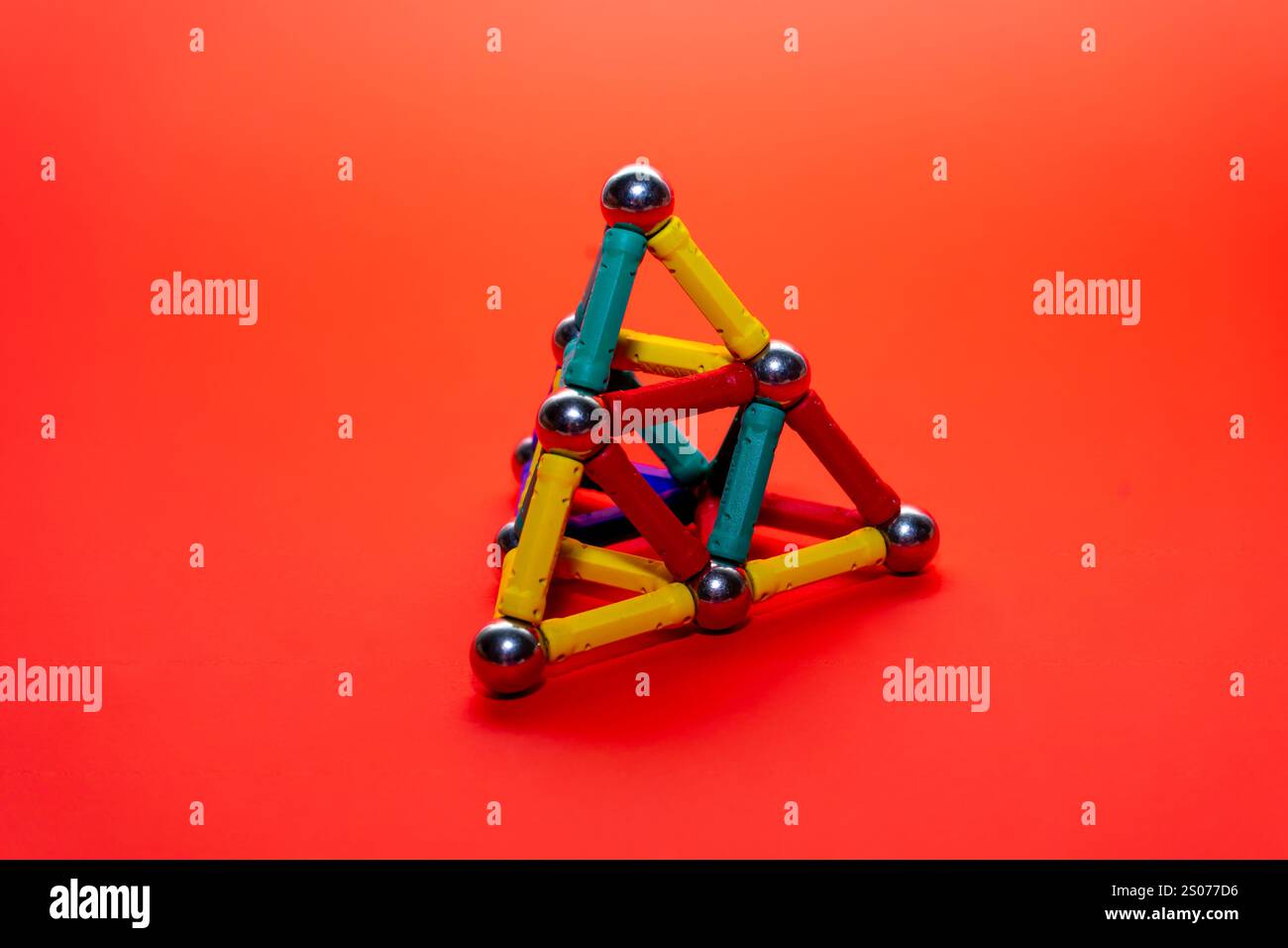Una struttura triangolare tridimensionale realizzata con vibranti bastoncini e sfere da costruzione magnetiche si appoggia su uno sfondo arancione brillante. Lo spettacolo del design Foto Stock