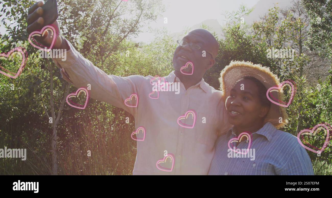 Immagine di cuori sopra una coppia afroamericana anziana che si fa selfie a natale Foto Stock