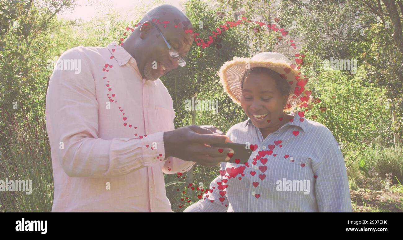 Immagine di cuori sopra una coppia afroamericana anziana che usa lo smartphone a natale Foto Stock