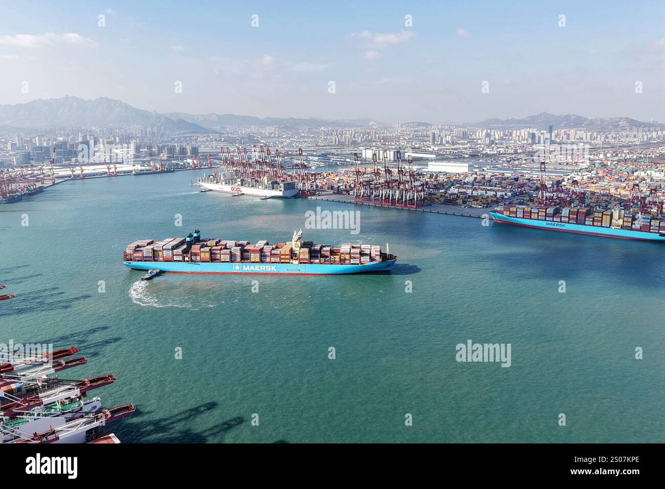 QINGDAO, CINA - 26 DICEMBRE 2024 - Una nave cargo carica di container per il commercio estero lascia il porto di Qingdao con l'assistenza di un rimorchiatore Foto Stock