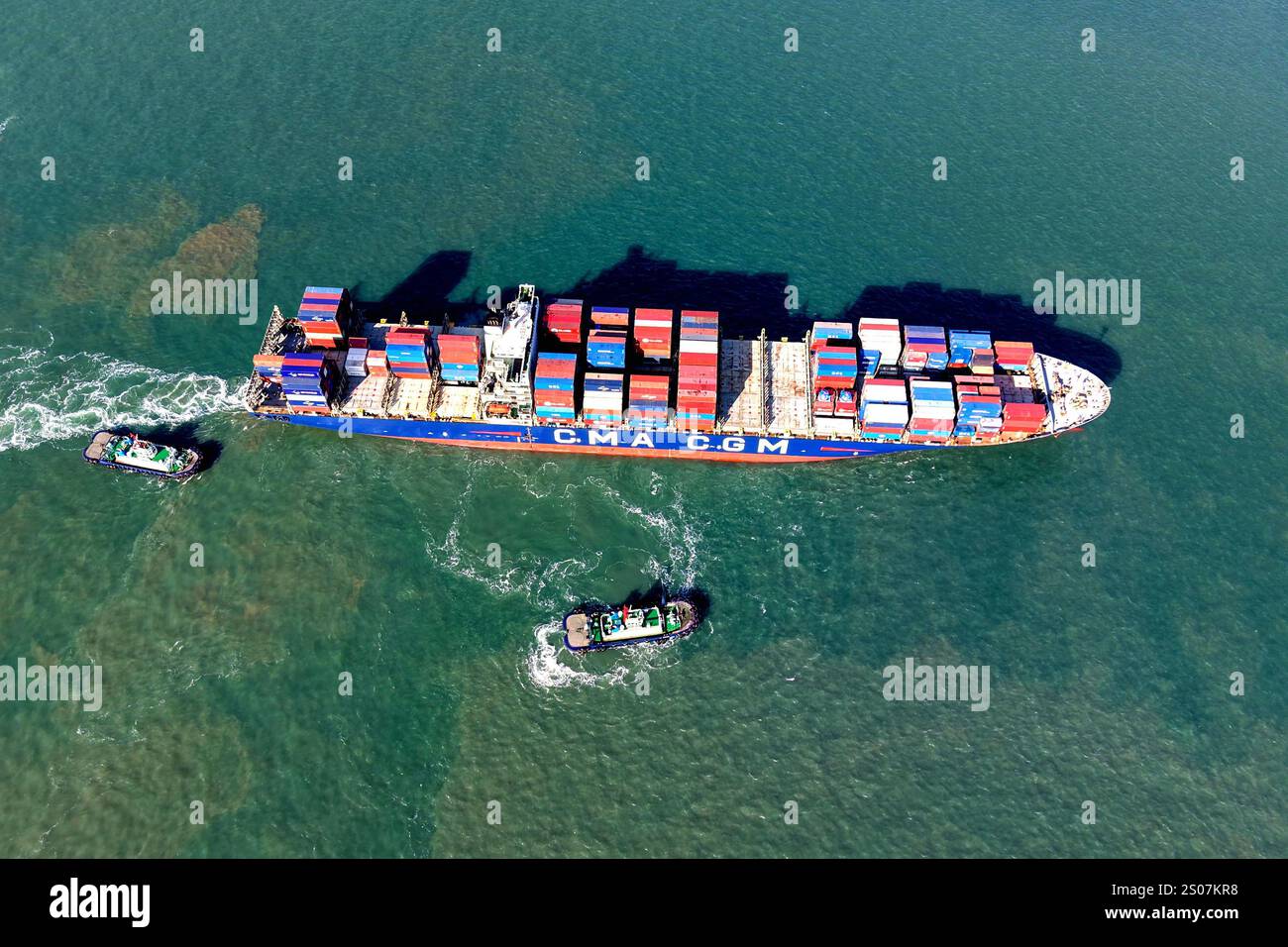 QINGDAO, CINA - 26 DICEMBRE 2024 - Una nave cargo carica di container per il commercio estero lascia il porto di Qingdao con l'assistenza di un rimorchiatore Foto Stock